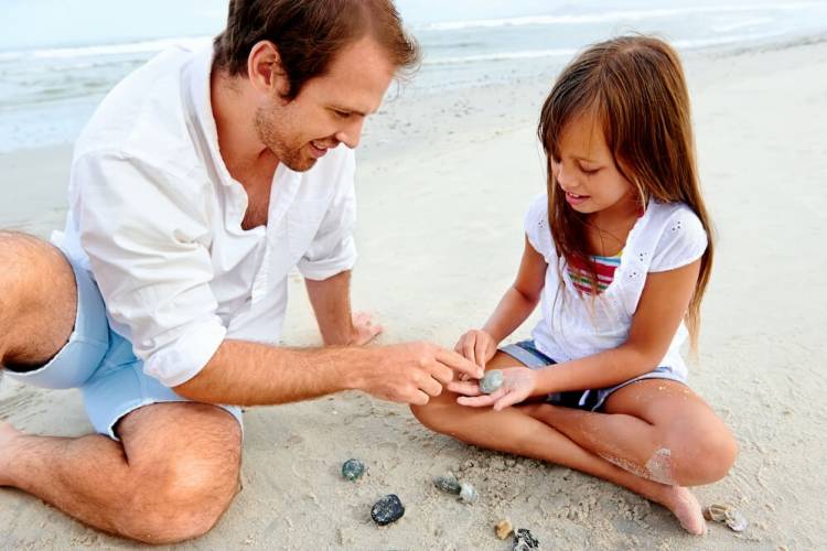 father and daughter on beach looking at shells