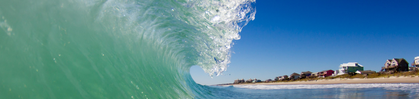 Light green shorebreak wave with homes in the background